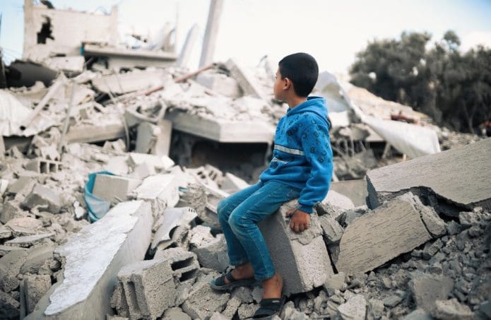 A young boy sits amid the rubble of a building destroyed by Israeli airstrikes in Gaza. (Shutterstock)