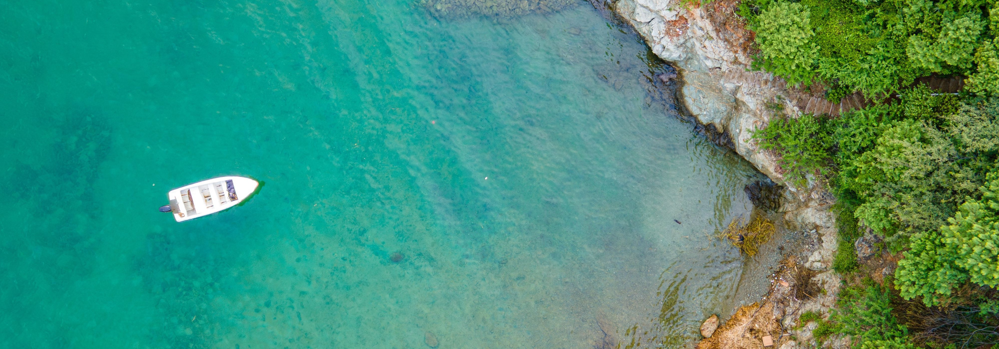 Photo: A boat floats in the Caribbean in light blue waters near a forested shore.