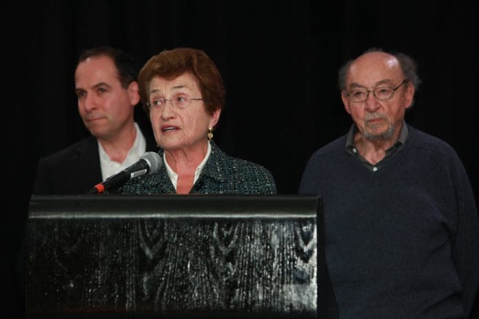 Cora Weiss speaks at a memorial event for the late Saul Landau in 2013. Her son Danny (left) and husband Peter (right) listen on.