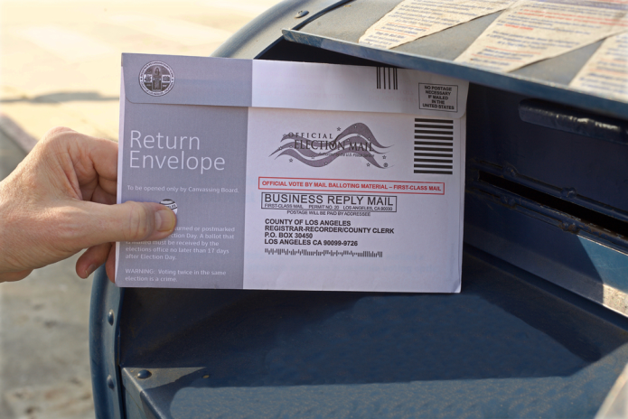 Photo of a hand placing a mail-in ballot in a mailbox