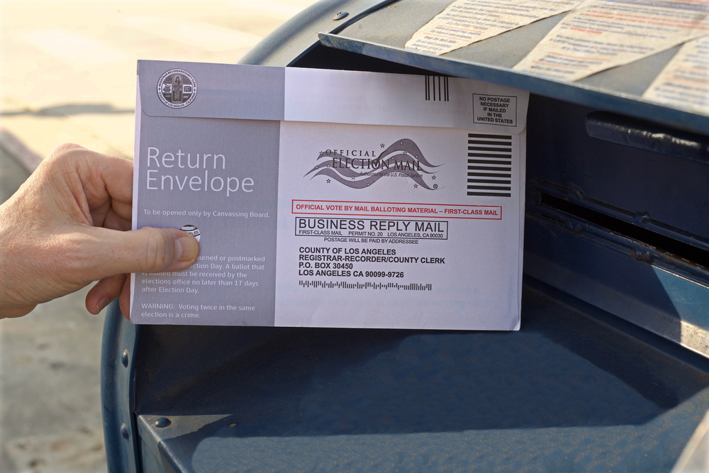 Photo of a hand placing a mail-in ballot in a mailbox