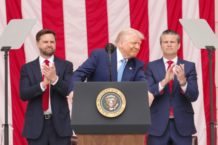 Photo of Donald Trump at a podium flanked by two other men with an American flag as a backdrop