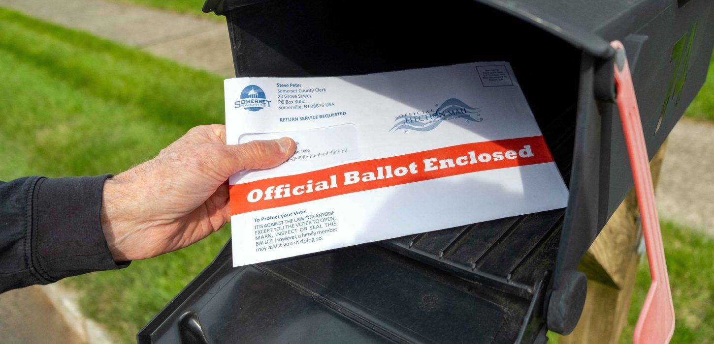 Photo of a hand placing an envelope labeled, "Official Ballot Enclosed," into a mailbox